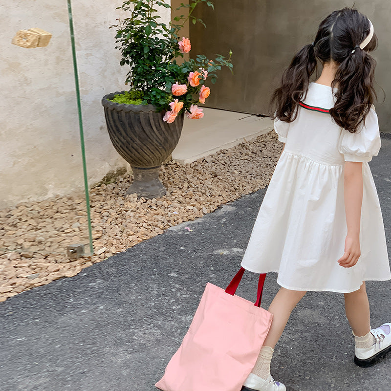 kid walking with white dress and red-trimmed tote bag